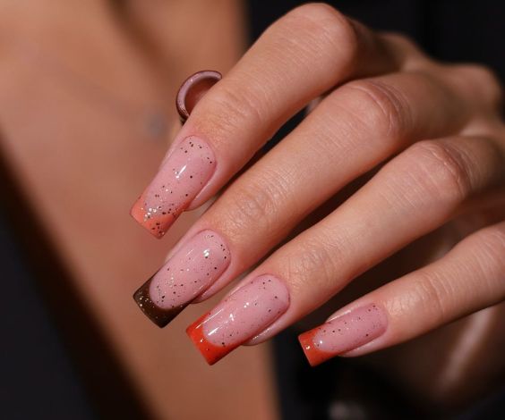 Orange and brown French tip nail art with glitter accents